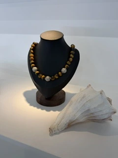 A warm-toned beaded necklace displayed beside a seashell